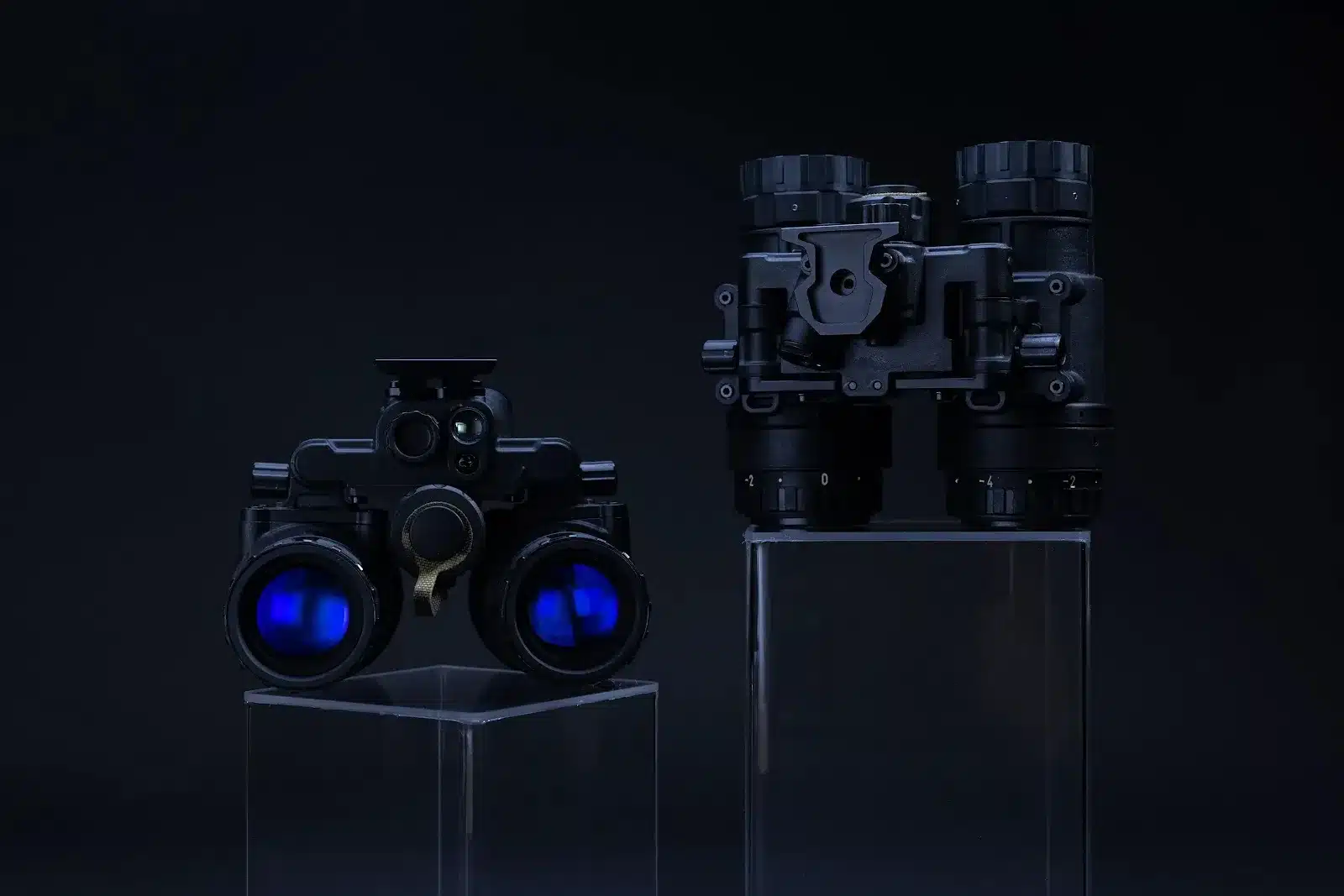 Two dual-tube night vision goggle systems displayed on clear acrylic pedestals with blue lens reflections.