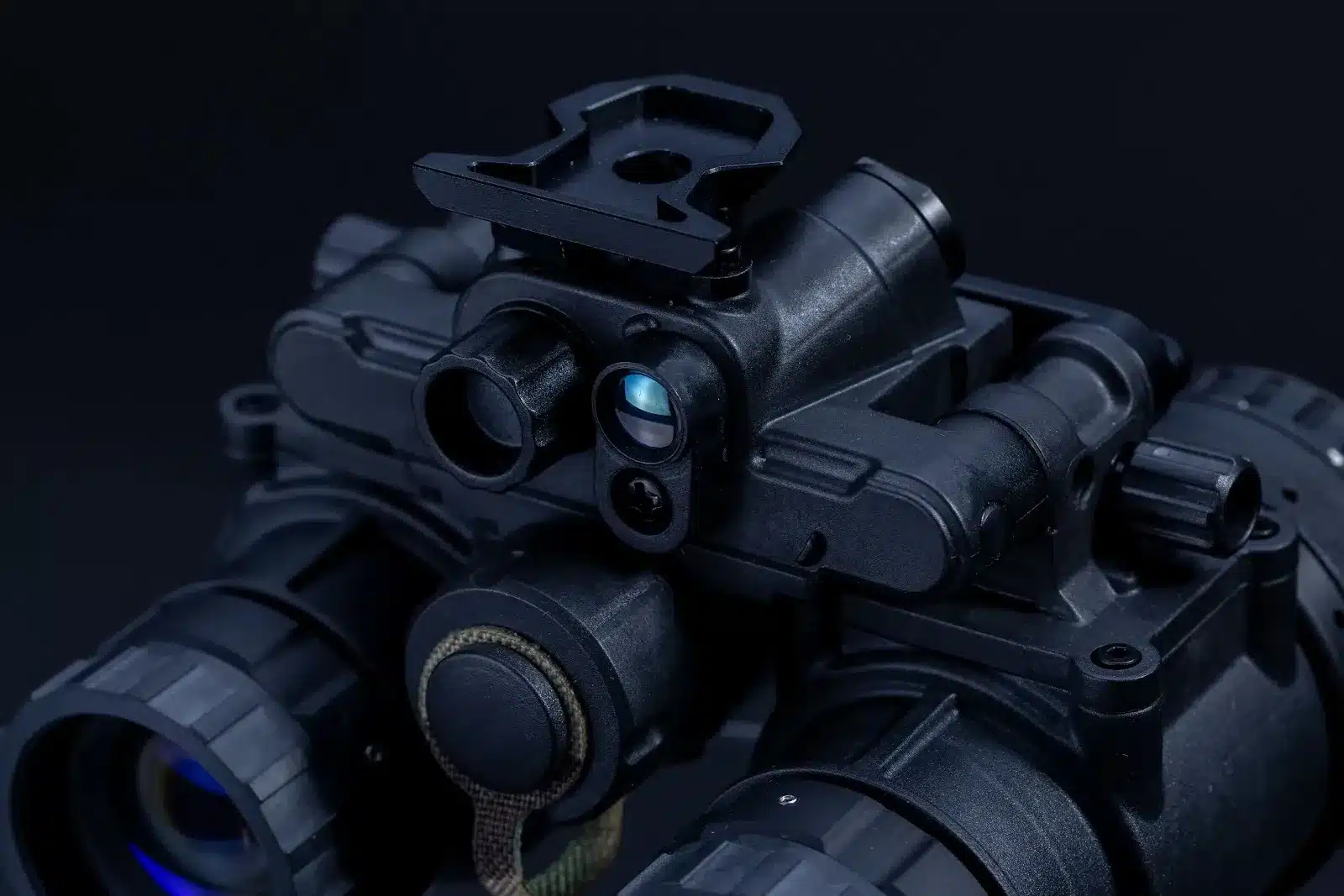Close-up of black dual-tube night vision goggles showing the top mounting assembly, battery compartment, and optical channels.